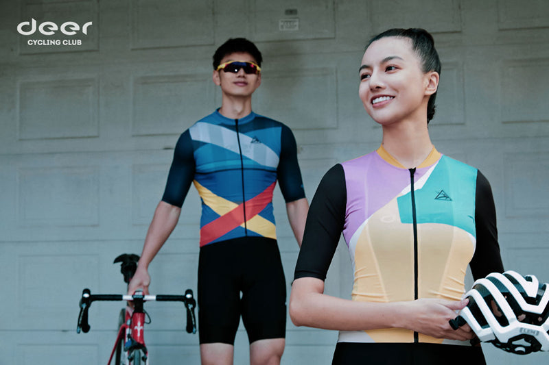 A woman wearing a DEER cycling jersey, with another rider behind.